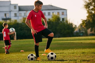 Formalı, şortlu ve kramponlu çocuk futbol oyuncuları çim üzerinde top oynuyorlar. Çocuklar sahada oynuyor. Futbol okulu. Spor anlayışı, sağlıklı yaşam tarzı, hobi, komutan, takım.