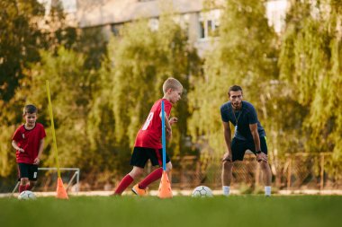 Çocuklar, futbol formalı futbolcular antrenmana hazırlanıyor, futbol sahasında topları var. Engellerle koşmak. Spor envanteri, egzersiz, boş zaman aktivitesi kavramı. Ad