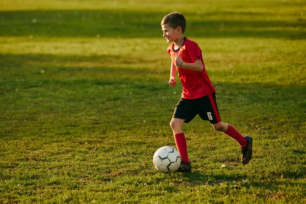 赤いスポーツユニフォームのボーイサッカー選手は 運動中のフットボールフィールドで試合のサイドラインからボールを投げます サッカーをする 子供のチームゲーム スポーツライフスタイル アクティビティ 趣味の概念 アドベンチャー — ストック写真