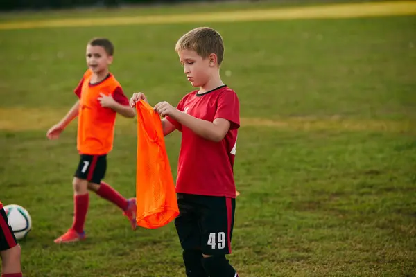 ボーイサッカー選手は 運動中のフットボール競技場で明るいオレンジ色のスポーツユニフォームを着用しています サッカーをする 子供のチームゲーム スポーツ トレーニング 健康的なライフスタイル アクティビティ 趣味の概念 — ストック写真