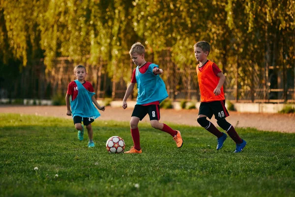 Forma ve kramponlarla koşan rekabetçi üç çocuk. Çocuklar futbol sahasında futbol oynarlar. Çocuklar okul takımı. Spor anlayışı, sağlıklı yaşam tarzı, aktivite, hobi. ad