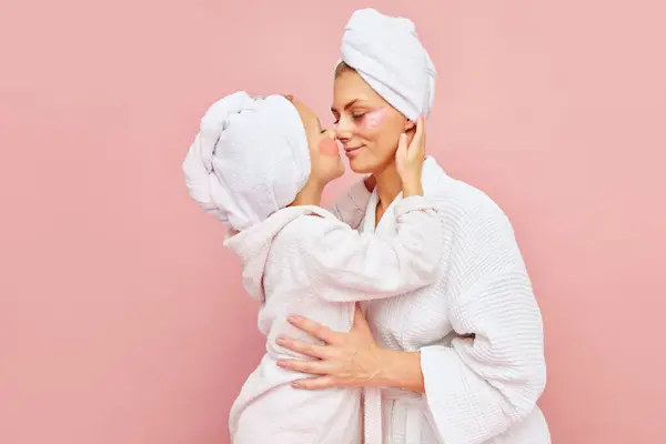 Motherhood. Loving mother and daughter in bathrobes and towels with eyepatches. Woman kissing her charming kid. Do beauty procedures together. Concept of beauty, spa treatment, natural cosmetic. Ad