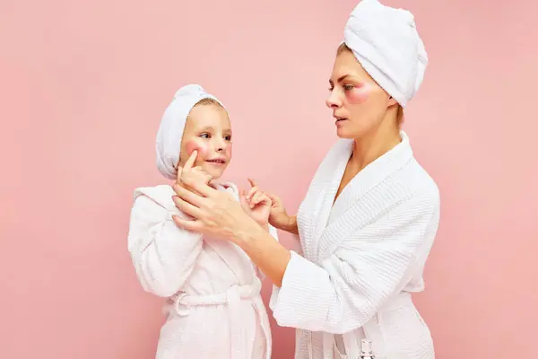 Home spa. Loving mother and daughter in bathrobes and towels using beauty product for skincare, eye patches. Women and child together care of beauty. Concept of beauty, family spa treatment, cosmetic.