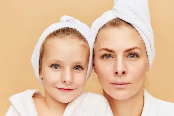 Close up portrait of mother and daughter in bathrobes looking at camera. Woman and child together care of beauty, health. Cosmetics and wellness of skin. Concept of beauty, spa treatment, self care,