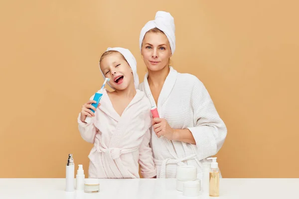 Portrait of lovely mother with daughter holding tooth brush near beauty table with cosmetic and hygiene products. Woman and kid together care of beauty, health. Concept of beauty, spa, wellness.