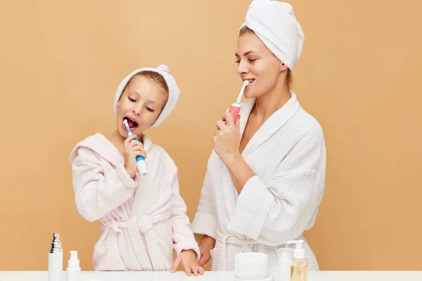 Portrait of lovely mother with daughter brushing teeth near beauty table with cosmetic and hygiene products. Woman and kid together care of beauty, health. Concept of beauty, spa, wellness, dental.