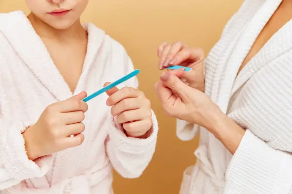 Cropped photo of mother and daughter hands filing nails in bathroom over beige backgrounds. Woman and kid together care of beauty, health. Concept of spa, wellness, pedicure, manicure, hygiene.