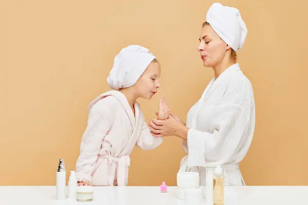 Portrait of lovely mother and daughter dry fingernail polish in bathroom over beige backgrounds. Woman and kid together care of beauty, health. Concept of spa, wellness, pedicure, manicure, hygiene.