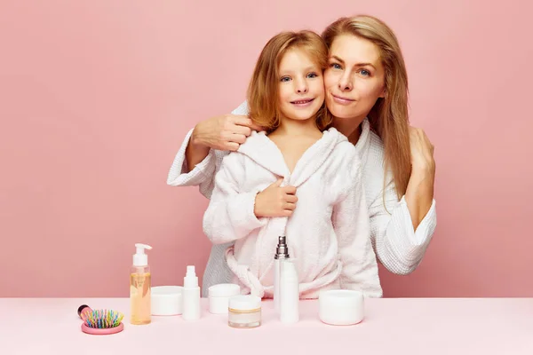 Portrait of mother hugging daughter in bathrobes looking at camera. Woman and child together care of beauty, health. Cosmetics and wellness of skin. Concept of beauty, spa treatment, self care,