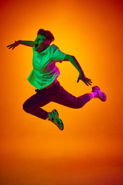 Sevinçten zıplamanın portresi, beyaz tişörtlü genç bir adamın gradyan turuncu arka planına bağırması, karışık renkleri aydınlatan neon ışığı. Gençlik kavramı, güzellik, moda, eğilimler, duygular, satış