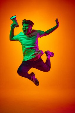 Beyaz tişörtlü hoparlörlü, hoparlörlü, turuncu arkaplanlı, karışık renkleri aydınlatan genç adam portresi. Gençlik kavramı, güzellik, moda, duygular, satış