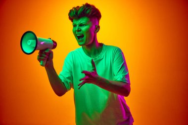 Genç adamın portresi hoparlöre bağırarak gradyan turuncu arka plana karşı satış sezonunun başlaması ve karışık renklerin aydınlatılması hakkında konuşuyor. Güzellik kavramı, moda, duygu, kazanmak