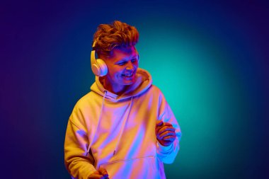 Genç adamın portresi, adamım, beyaz kapüşonlu giyinmiş, kulaklıkla müzik dinleyen karışık renkli neon filtreli naneli arka plan. Duygular, moda, tarz, trendler, dans. ad
