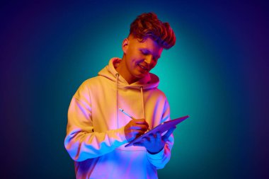 Neşeli adamın yakın portresi, beyaz giysili bir öğrenci elinde tablet, ve neon ışıklarıyla arkaplandaki değişime karşı notlar tutuyor. Tarz kavramı, online çalışma, bilişim uzmanı, çalışma. ad