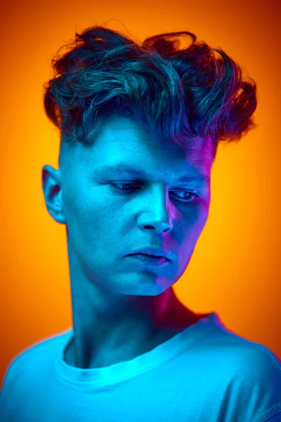 stock image Close up portrait of young handsome man, student looking away against gradient orange background illuminated blue color neon light. Concept of beauty, youth, self expression, human emotions. Ad