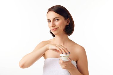 Neşeli, güzel, genç bir model, omuzları açık, beyaz arka planda reklam kremi olan bir kadın. Yakın çekim. Güzellik kavramı, moda, cilt bakımı, duygular. Model mutlu, heyecanlı görünüyor.