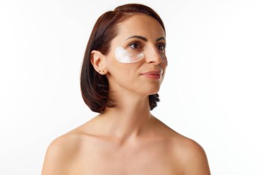 Çıplak omuzlu, beyaz stüdyo arka planında yamaları olan çekici esmer bir kadının portresi. Güzellik anlayışı, doğal makyaj, cilt bakımı, sağlıklı görünüş, sabah prosedürleri, reklam