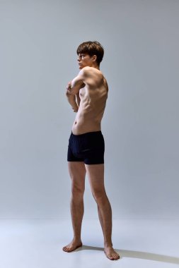 Gri stüdyo arka planında izole edilmiş kaslı erkek vücudunun tam boy portresi. İç çamaşırlarıyla poz veren genç bir adam. Erkeklik. Güzellik, moda, spor, vücut ve cilt bakımı, sağlık. ad