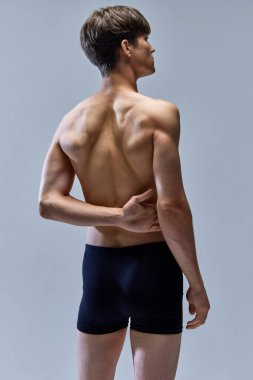 Genç yakışıklı bir adam, erkek model. Gri stüdyo arka planında izole edilmiş iç çamaşırlarıyla poz veriyor. Kas yapısı geri geldi. Güzellik, moda, vücut ve cilt bakımı, sağlık, erkeklik kavramı. ad