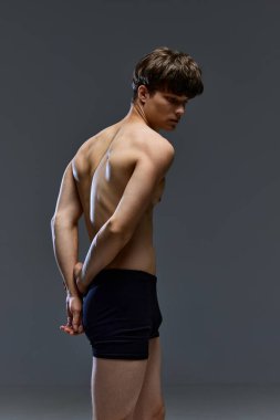 Gri stüdyo arka planına karşı iç çamaşırlarıyla antik bir heykel gibi poz veren kaslı üstsüz bir gencin arka plan portresi. Erkeklik. Gençlik kavramı, erkek sağlığı, doğal güzellik, sağlık. ad