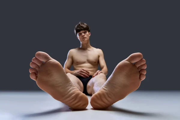 Bare foot of muscular shirtless young man posing, lying on floor in underwear against grey studio background. Pedicure, hygiene. Concept of youth, mens health, natural beauty, wellness. Copy space.