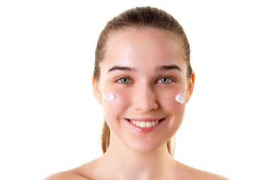 Çıplak omuzlu, cilt bakım kremi sürmüş beyaz stüdyo arka planında kameraya bakan genç kızın portresini yakından çek. Doğal güzellik, spa, kozmetoloji, duygu konsepti