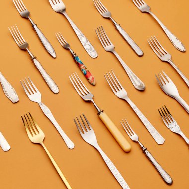 Çatal bıçak. Paslanmaz çelikten, gümüşten ve altın çatallardan oluşan üst düzey manzara turuncu stüdyo arka planına göre simetrik olarak düzenlenmiştir. Mutfak, antika, retro, tatil, sofra kurma kavramı