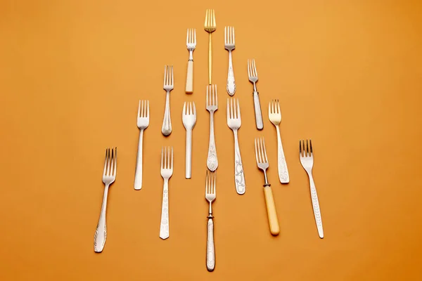Cutlery. Pop art style. Flat lay of variety of stainless steel, antique silverware and gold forks arranged over orange studio background. Concept of kitchen, vintage, retro, holiday, table setting