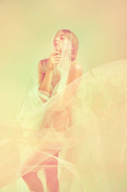 Gözleri kapalı, şeffaf kumaşla tek başına duran genç ve güzel bir kadın. Retro pastel renk paleti. Kadın vücut konseptinin doğal güzelliği. Vurgulama etkisi