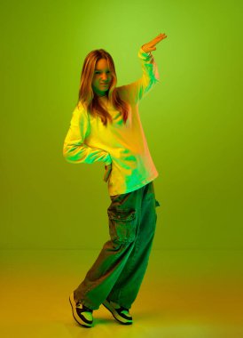 Sevimli çocuk, kız, dans eden öğrenci ve stüdyo arka planında karışık renklerde kameraya bakan neon ışığın tam boy portresi. Mutluluk kavramı, yüz ifadesi, satış, tatil.