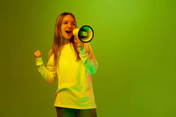 Pretty child, girl, student shouting to megaphone of happy and enjoy in mixed colors neon light. Concept of happiness, facial expression, emotions, sales season, shopping, holidays. Copy space. Ad