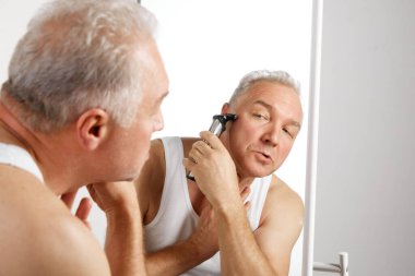 Çekici gülümseyen orta yaşlı bir adamın portresi aynaya bakıyor ve tıraş olurken tıraş oluyor. Doğal güzellik kavramı, cilt ve yüz bakımı, yüz ifadesi, hijyen. Uzayı kopyala Ad