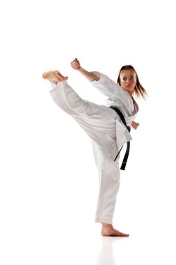 Beyaz üniformalı genç bir kadın dövüş sanatları eğitimi alıyor. Beyaz stüdyo geçmişinden izole edilmiş. Profesyonel spor, eğlence, sanat, hobi, kültür kavramı. İlan, metin için boşluk kopyala.