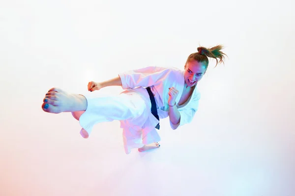 Top view portrait of karate fighter, master, woman performing high kick isolated over white studio background. Concept of professional sport, recreation, art, hobby, culture. Copy space. Fish eye.