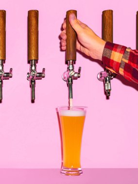 El yapımı hafif birayı soğuk bardağa döküyordu. Bira, pembe arka planda köpürerek fincana dönüşür. Bira, alkol, iyi zamanlar, Cuma havası, Ekim Festivali.