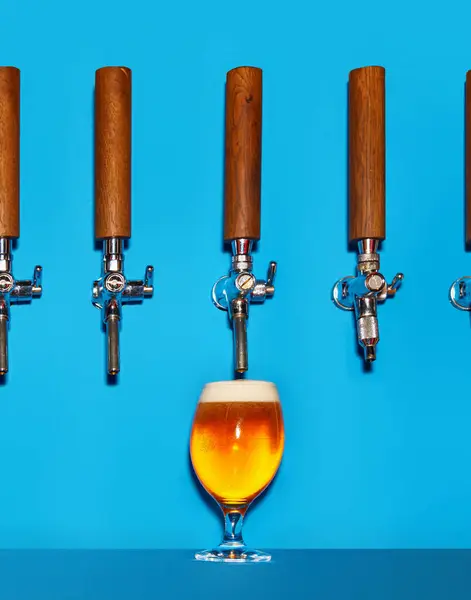Golden cold beer pouring from tap into chilled glass. Drink forms thick, foaming pours into mug against blue background. Concept of beer, alcohol, good times, Friday mood, Oktoberfest