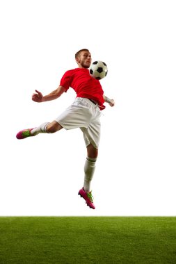 Genç bir adam, kırmızı spor giyimli profesyonel bir futbolcu ve yeşil çimenli beyaz arka plana karşı futbol numaraları yapıyor. Oyun, spor, eğlence, aktif yaşam tarzı kavramı.