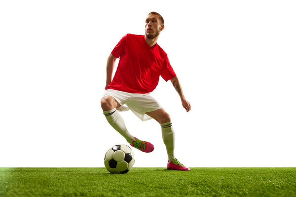 Professional soccer player looks confident in sportwear and boots training kicking ball for goal in jump against white background. Football school. Concept of game, sport, recreation, active lifestyle