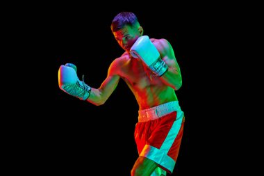 Genç adam, eldivenli profesyonel boksör. Siyah modda arka planda karışık neon filtresi ve ışık var. Spor anlayışı, aksiyon, hareket, sağlıklı yaşam tarzı. İlan için alanı kopyala.