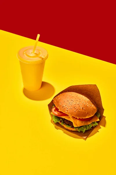 Packing food boxed take away. Tasty hamburger with beef sauces and vegetables with refreshing drinks against vivid red-yellow background. Concept of fast food, delivery menu, catering. Copy space