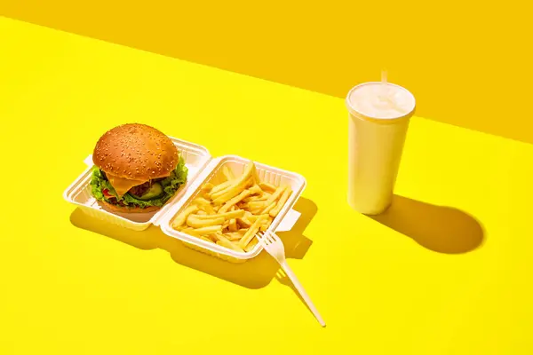 Unpacking tasting fast-food. hamburger with soda and fried potato in paper boxes against vivid yellow background. Concept of junk food, menu, delivery, catering, take away. Copy space