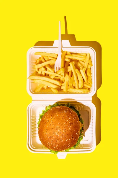 Unpacking tasting fast-food. Top view of hamburger and fried potato in paper boxes against vivid yellow background. Concept of junk food, menu, delivery, catering, take away. Copy space for text. Ad