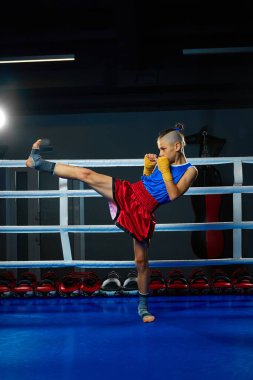 Küçük atletik bir çocuğun tam boy portresi, spor kulübündeki dövüşten önce ringde profesyonel MMA sporcusu eğitimi. Spor anlayışı, sağlıklı yaşam tarzı, hobi, spor, yarışma.