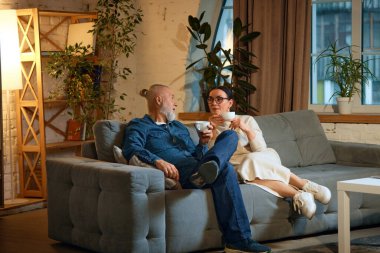 Mutlu yaşlı bir çiftin portresi kanepede oturuyor, karı koca çay içerken dinleniyor ve evde konuşuyor. Aşk kavramı, emeklilik hayatı, hafta sonu, emekliler, rahat, kış tatili.