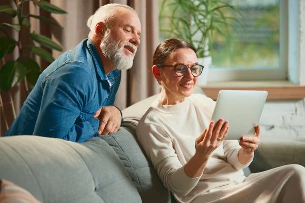 Mature couple, senior people sitting on couch and choosing household product in tablet in internet shop. Shopping online. Concept of love, retirement life, pensioners, cozy, winter holidays, sale.