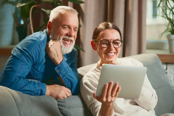 Lovely, elderly people, mature couple relaxing on sofa in living room and using digital tablet. Technology, elderly man or senior woman Concept of love, retirement, pensioners, cozy, winter holidays.