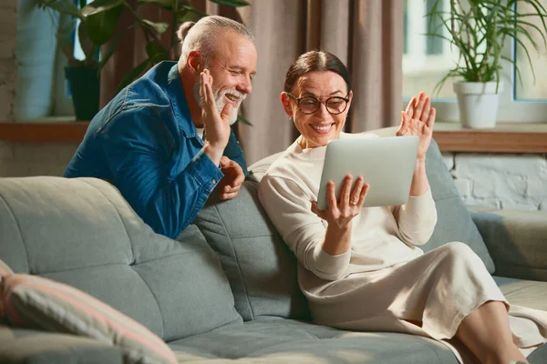 Side view portrait of old lovely couple elderly man and senior woman with tablet while online chatting or on video call with greeting. Concept of love, retirement life, pensioners, winter holidays.