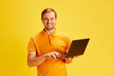 Genç, çekici bir adamın portresi, zeki çocuk, dizüstü bilgisayar tutan ve çalışırken kameraya bakan ya da izole edilmiş sarı stüdyo geçmişini inceleyen bir öğrenci. Yüz ifadesi kavramı, insani duygular. Ad