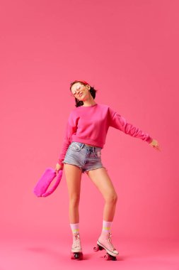 Modern pembe aksesuarları olan tam uzunlukta genç bir kadın klasik paten üzerinde duruyor izole edilmiş canlı stüdyo arka planı. Gençlik kavramı, moda, tarz, olumlu insani duygular.