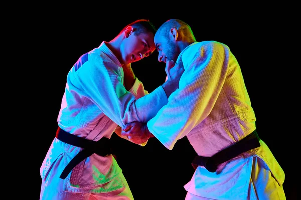 Side view portrait of two man looking eyes to eye while fighting in neon light isolated black background Concept of martial art, combat sport, health, strength, energy, fit. Copy space